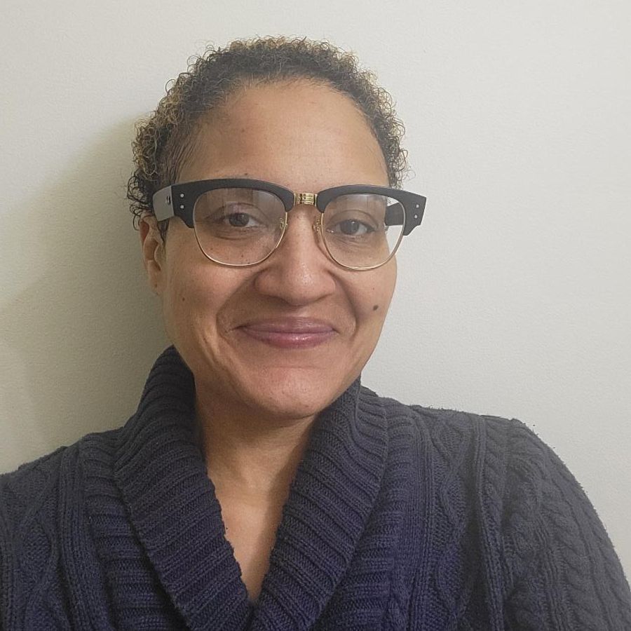 Headshot image of Blaire Hines. She wears glasses, a navy sweater and is against a white/gray background.