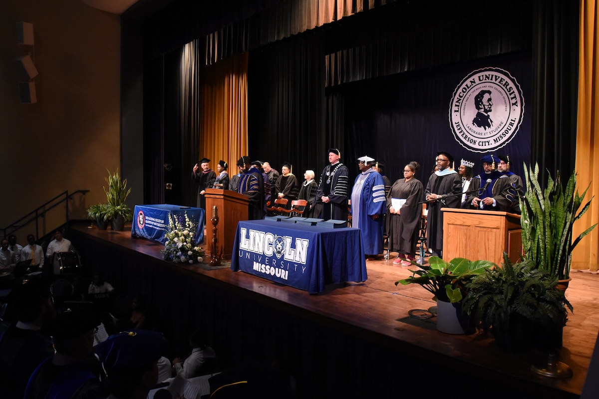 Lincoln University of Missouri faculty and staff stand on a stage while wearing robes and university regalia during the 2025 Honors Convocation ceremony.