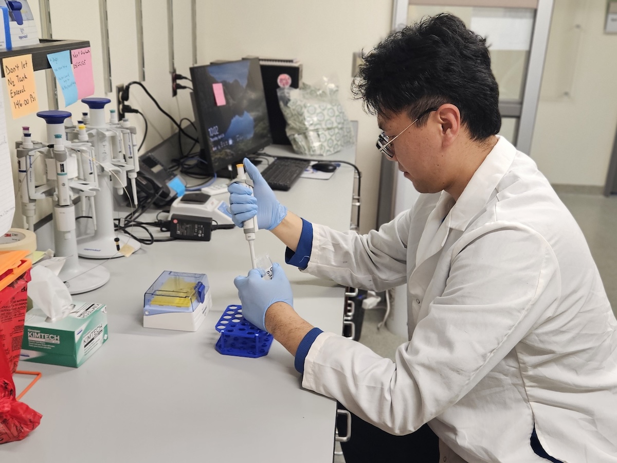 A young man in a lab coat uses chemistry equipment in a small laboratory. 