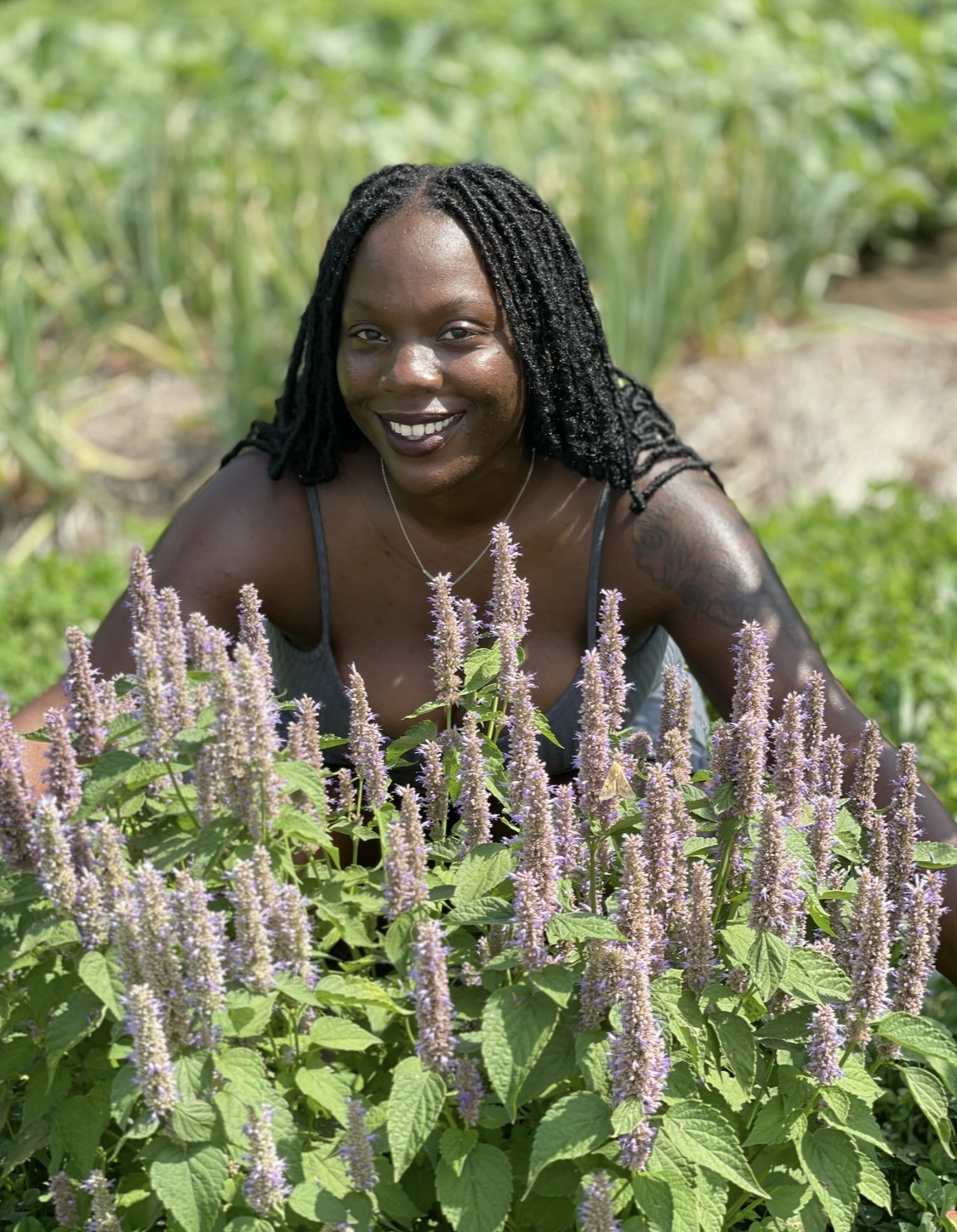 Julia Thompson, an outreach worker with ISFOP, smiles beside a healthy patch of anise hyssop — a pollinator-friendly herb known for its fragrant purple flower spikes and minty aroma.