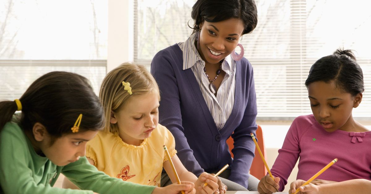 Teacher smiles while assisting a diverse group of young students with a classroom activity, representing education and learning.