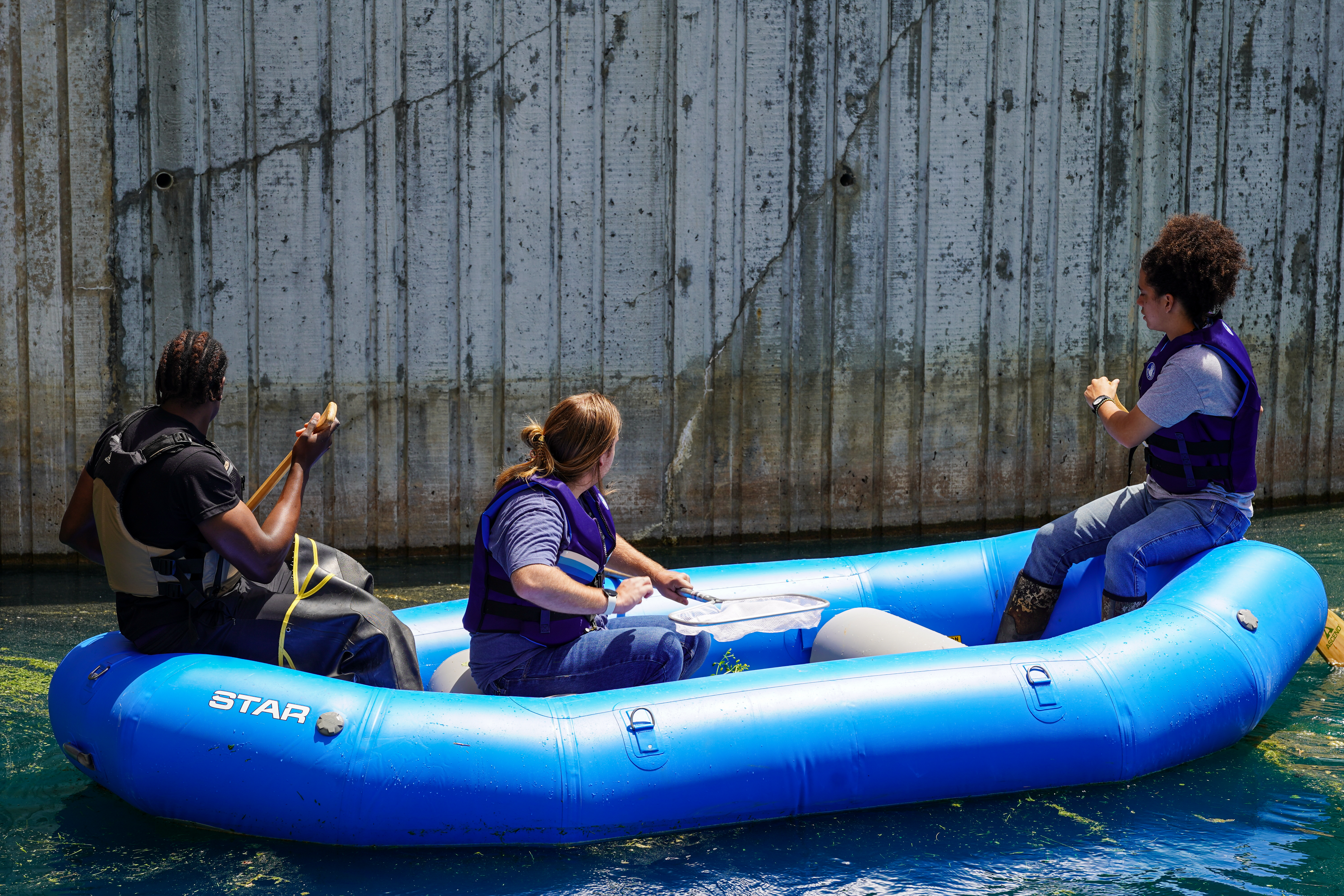 Three young men paddle an inflatable boat in a pond. 