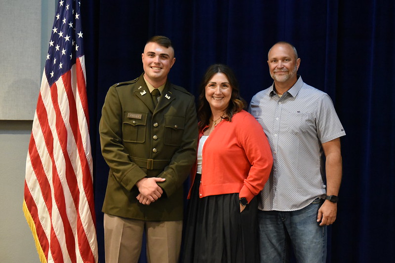 Cadet Blake Fischer and his parents pose for a picture on stage with an American flag in the background.