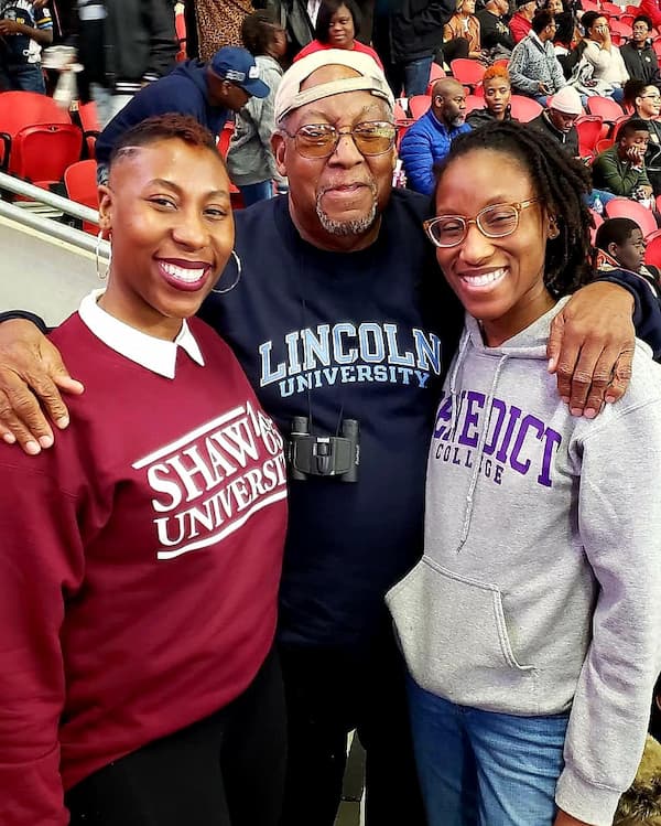 Robert Sams Jr. stands with two of his daughters. They all wear HBCU sweatshirts.