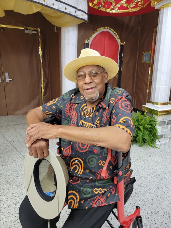 Robert Sams Jr. sits in a wheelchair while wearing a patterned button up shirt and a hat.