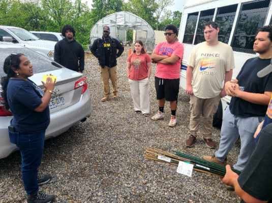 Dr. Chitturi stands near a vehicle holding a sticky trap while addressing a group of students.