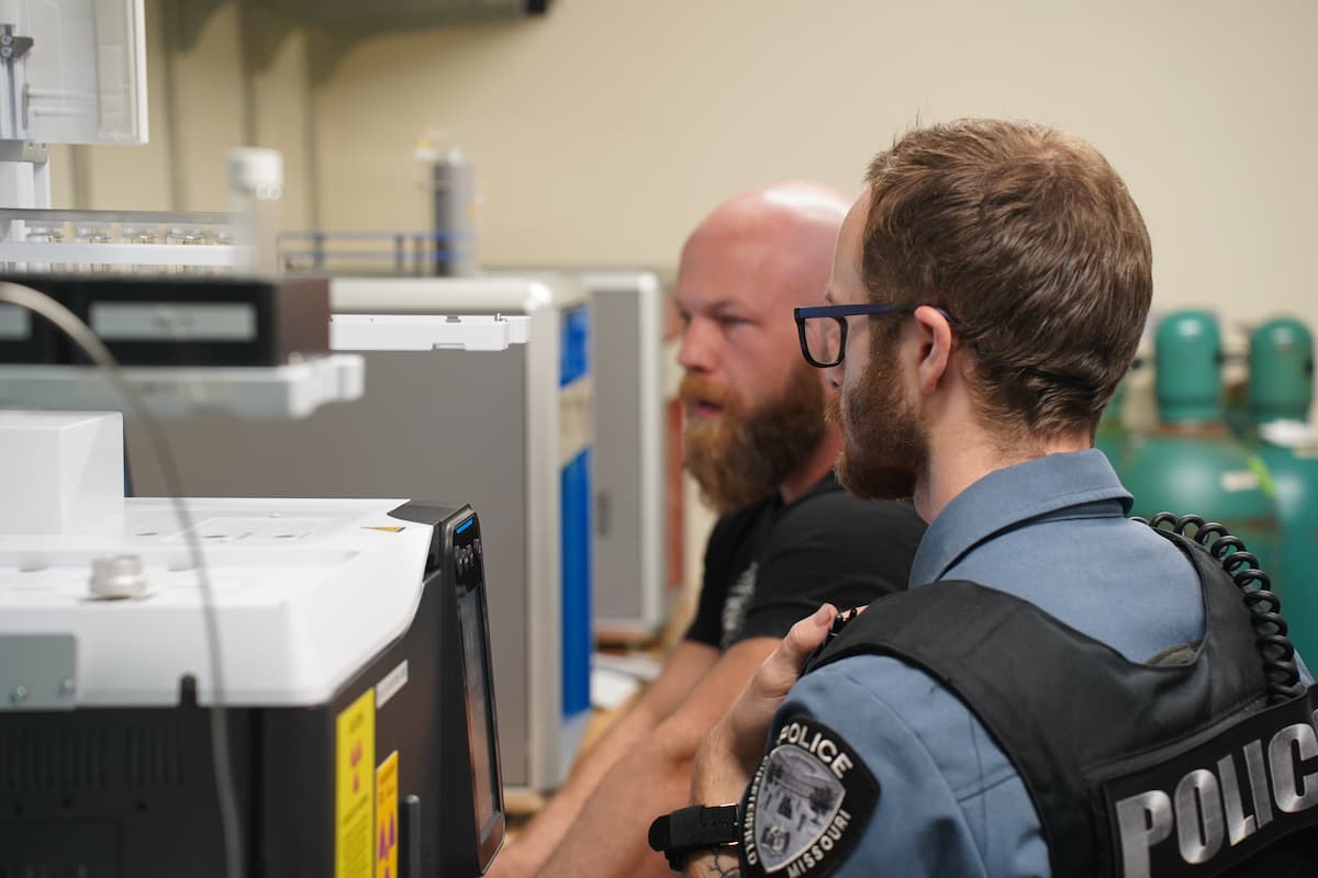 A man and a police officer stand in front of a piece of science equipment.