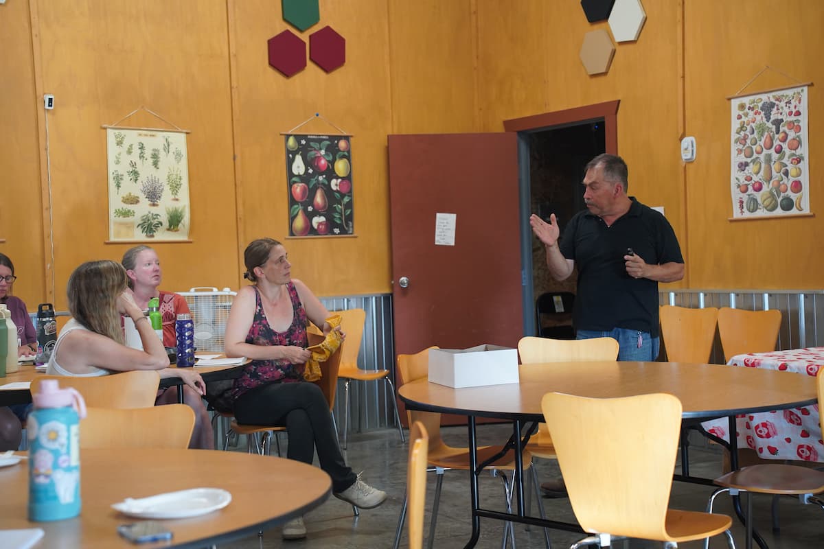 A standing man speaks to a group of seated people in a small classroom. 