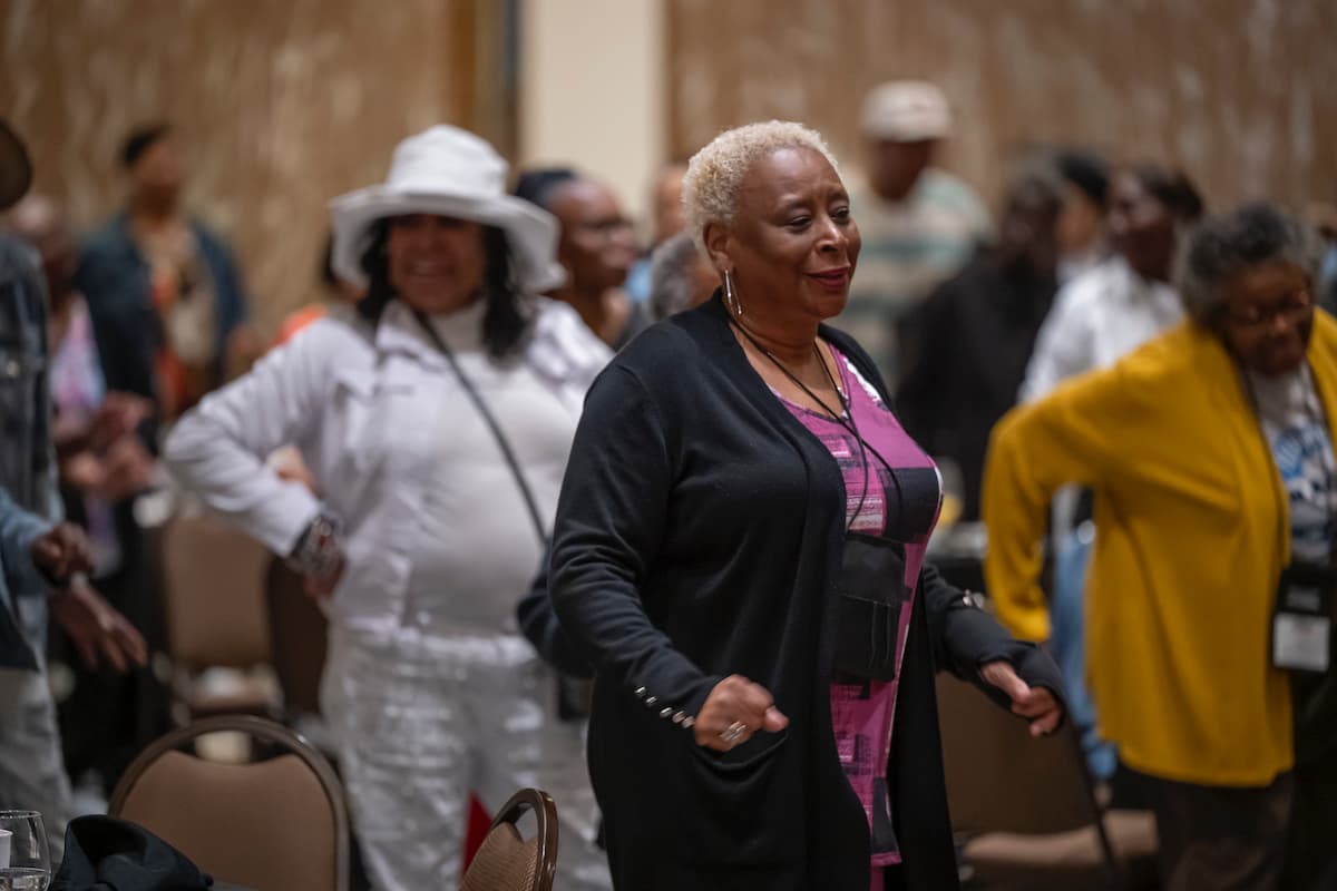 Women stand and dance during a conference workshop in a conference room.