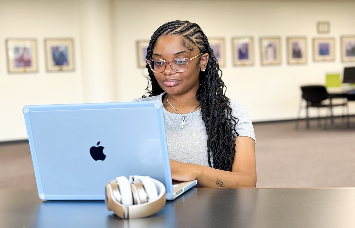 A young woman works on her laptop while sitting at a table. 