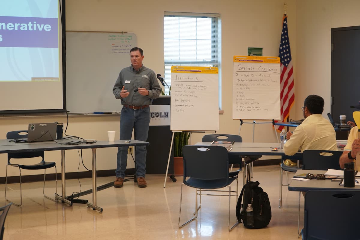 Man stands at the front of a classroom next to two note pads on easels. 
