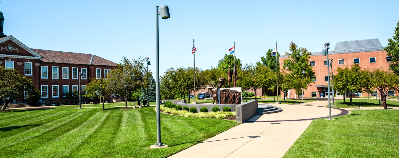 Lincoln University campus green with Soldiers’ Memorial Plaza, flags, and historic red-brick buildings under a clear blue sky