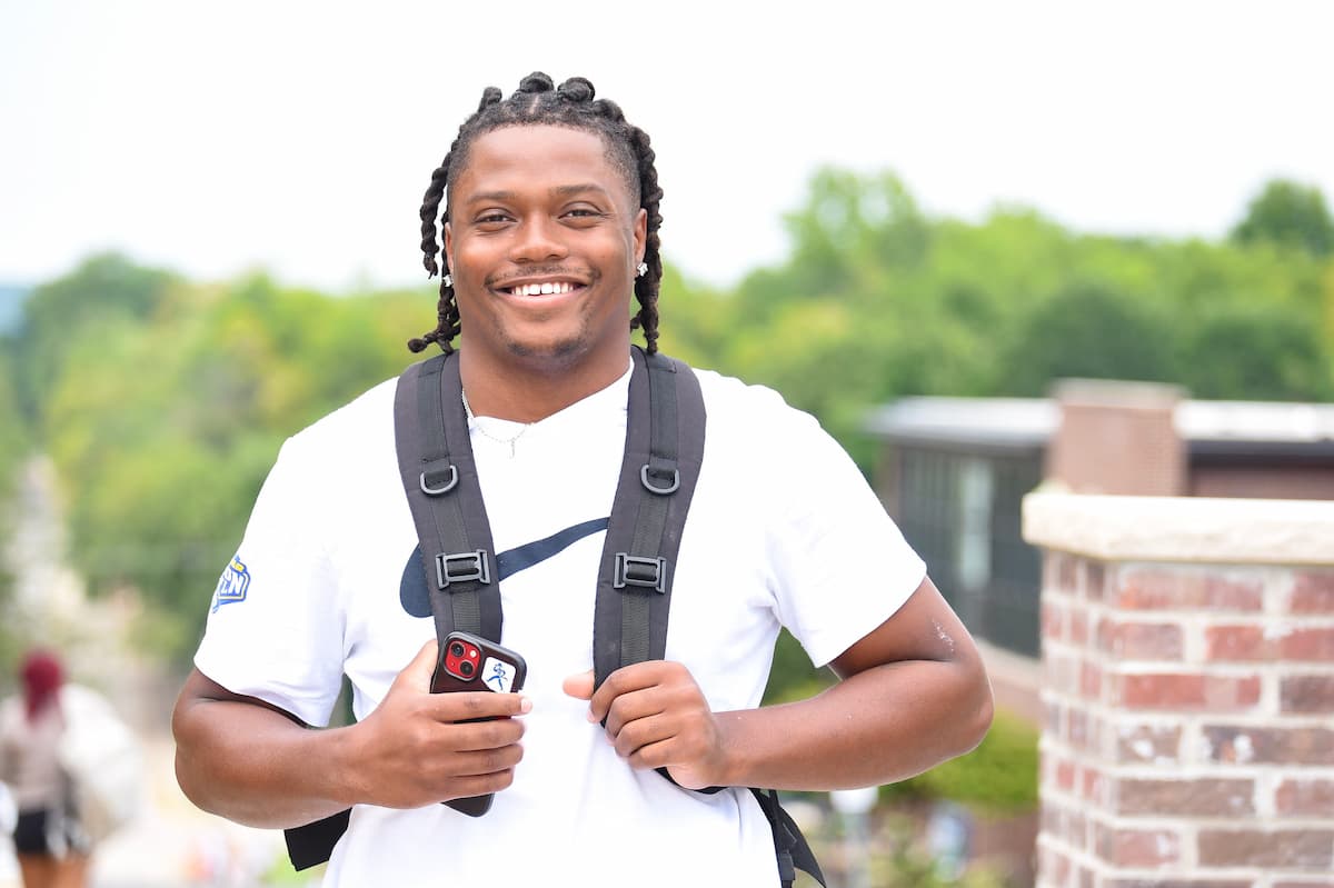 Image of a male student in a white shirt with a backpack on his back standing on the Lincoln University campus.