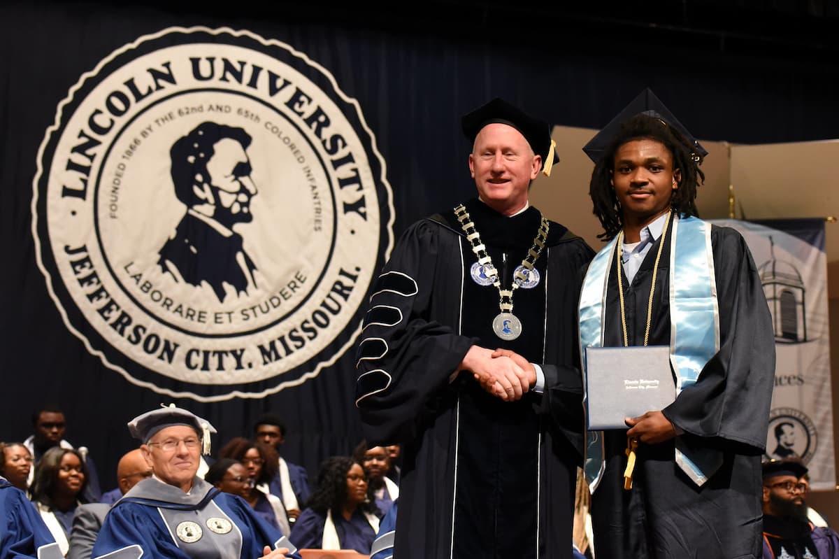 Lincoln Univeristy President shakes hands with a student while on stage during a graduation ceremony. 