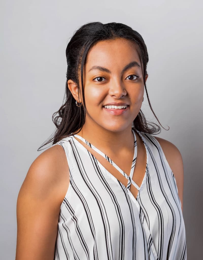 Headshot image of Hosanna Tesfaye. She has dark hair and is wearing a sleeveless striped blouse. 