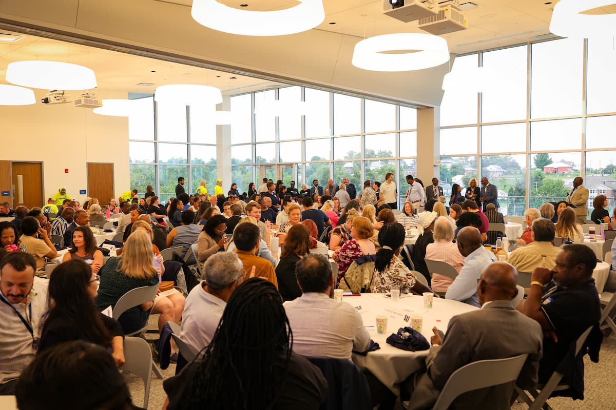 A large group of people sit at various round tables in a conference room.