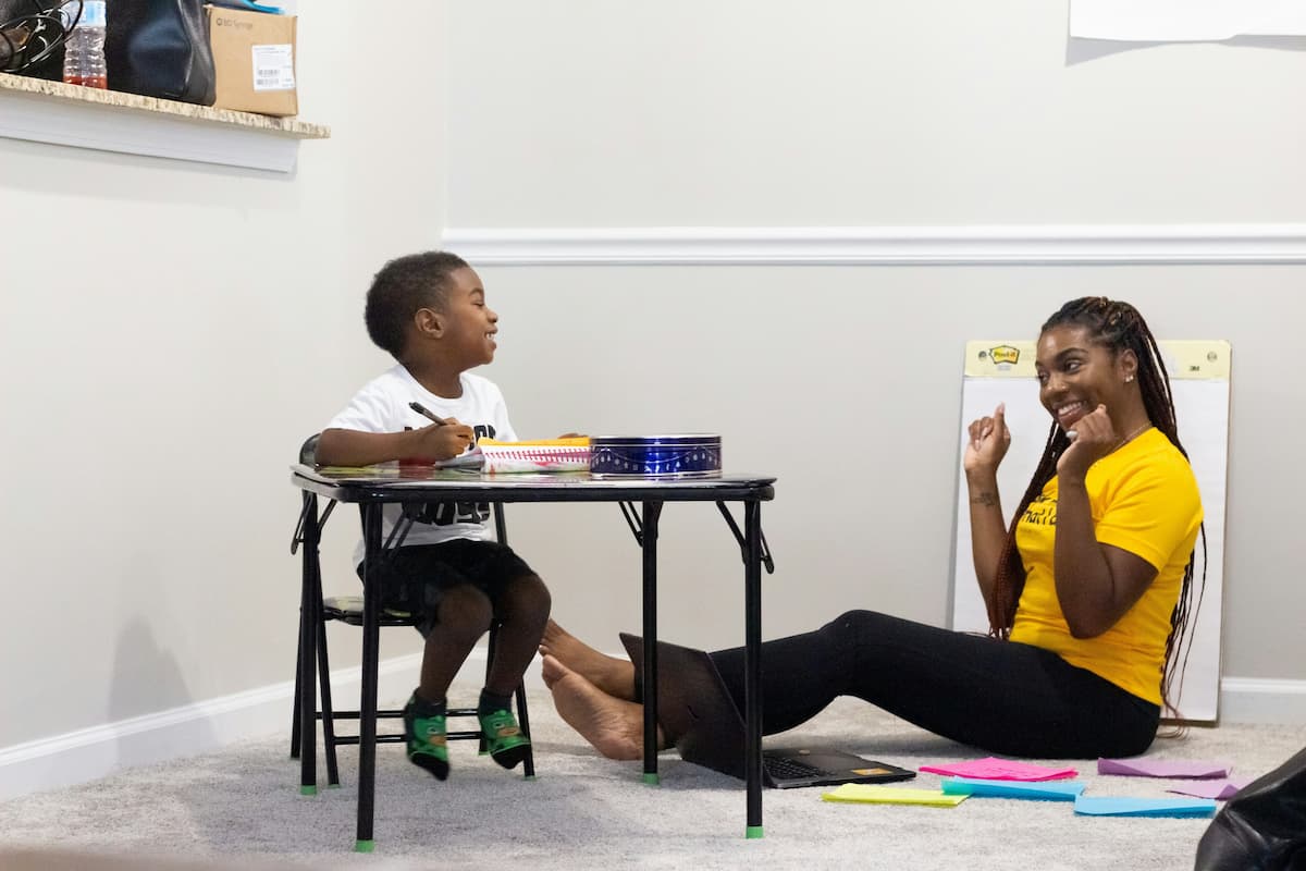 A young woman sits on the floor with a small child while playing.