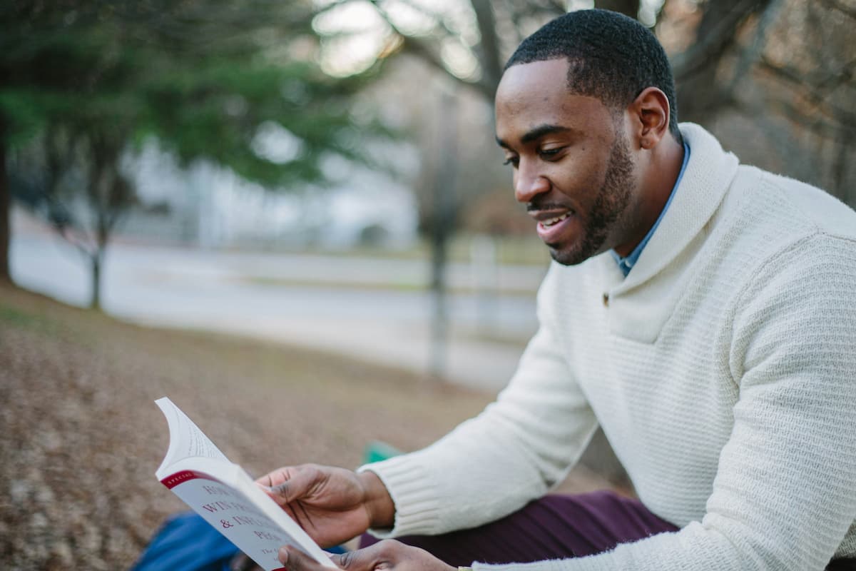 A young man sits outside while reading a book.