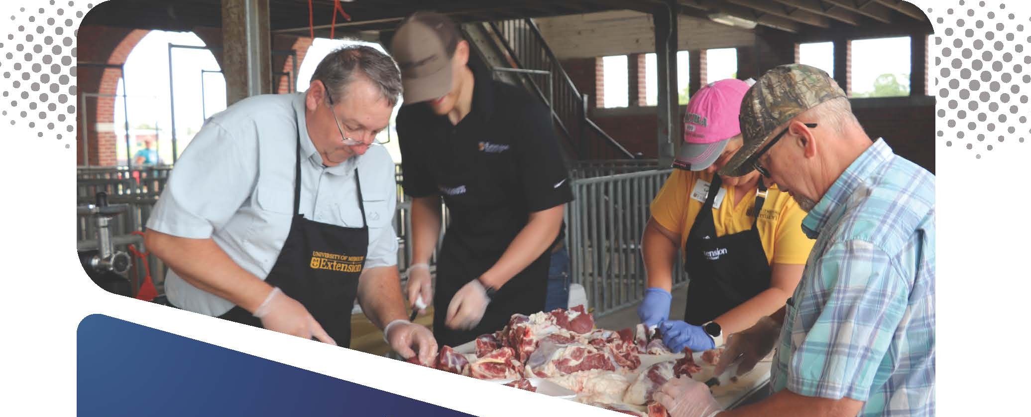 Four individuals, wearing aprons and gloves, work together to process raw meat on a table in an indoor facility. Two of the aprons display "University of Missouri Extension" branding.
