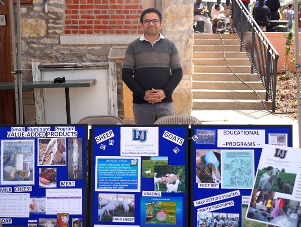 Dr. Mohan Acharya stands by his Small Ruminant Program display on sheep and goat farming at an outdoor event booth.