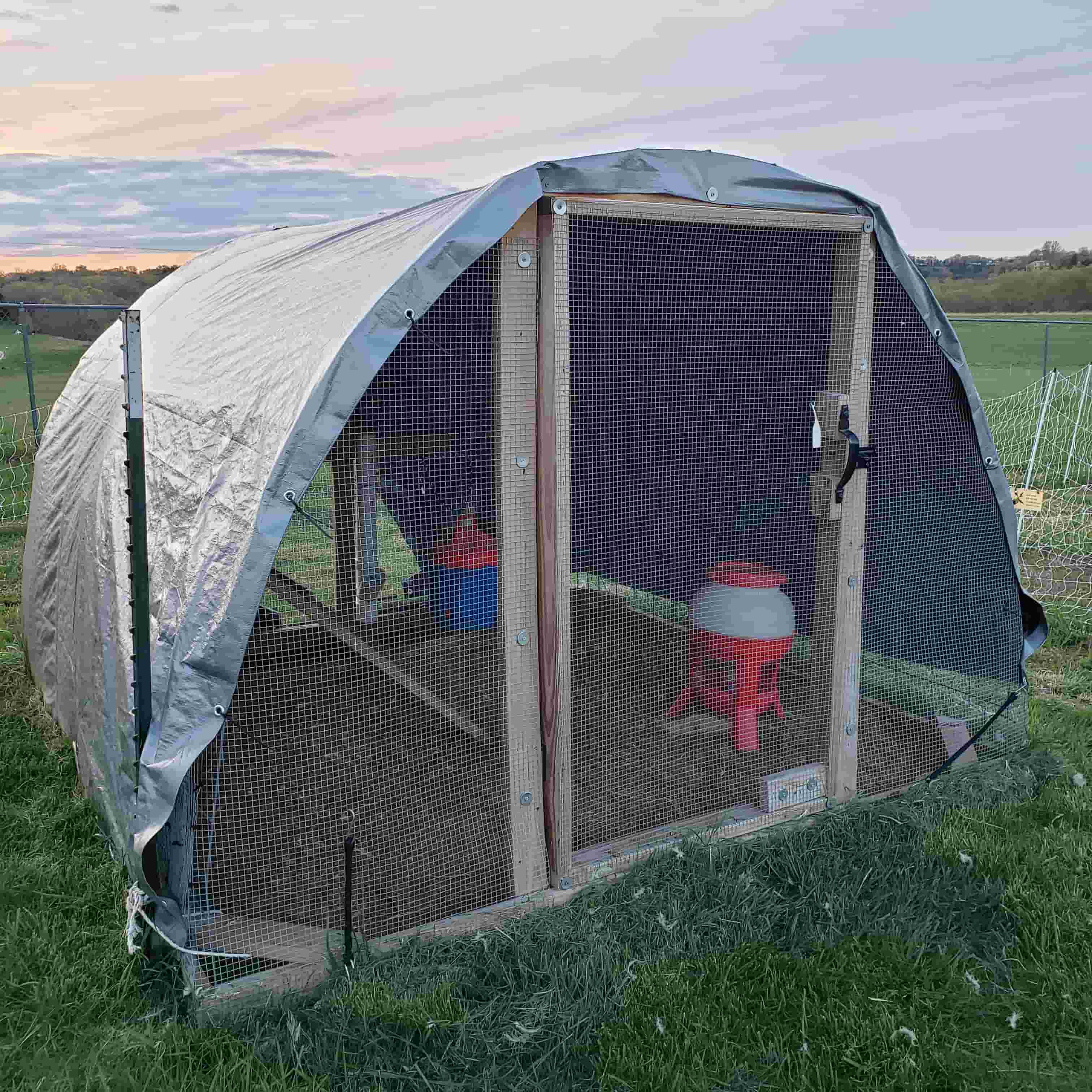 Hoop-style poultry coop with a curved tarp roof, screened front entrance, and feeders inside at Lincoln University's Carver Farm.