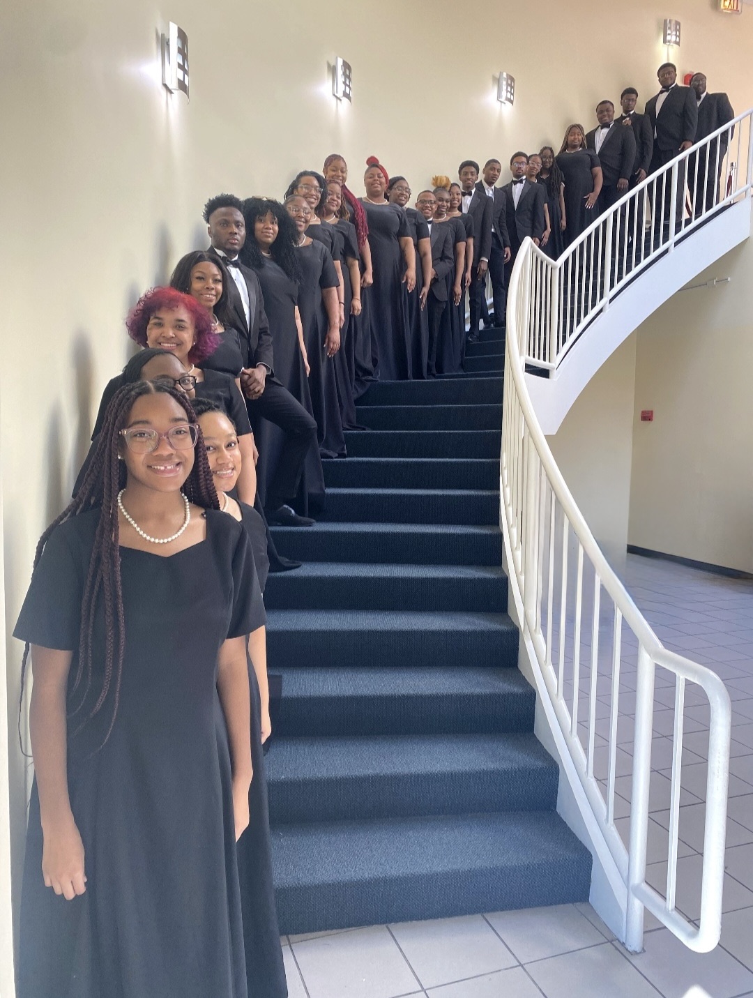 The Lincoln University of Missouri choir poses for a photo up a curved staircase with blue steps and a white rail. 