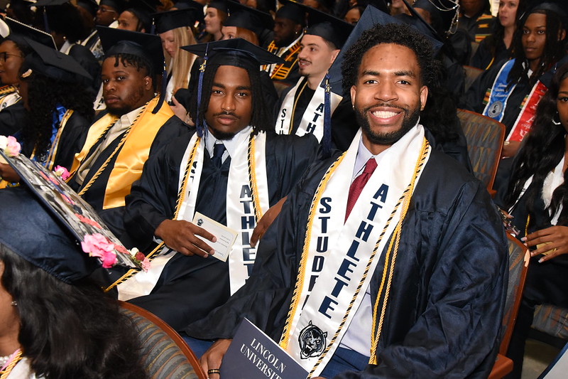 Lincoln University of Missouri student-athlete graduates sit in the auditorium in their graduation regalia.