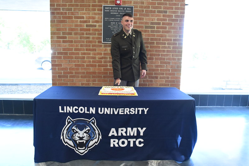 Cadet Blake Fischer stands in the foyer cutting his celebratory cake following his commissioing ceremony.