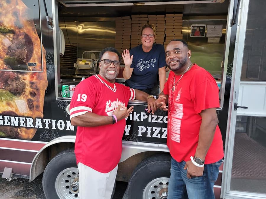 Two Lincoln University of Missouri male alumni in red shirts lean into a food truck during a Lincoln University Homecoming event.