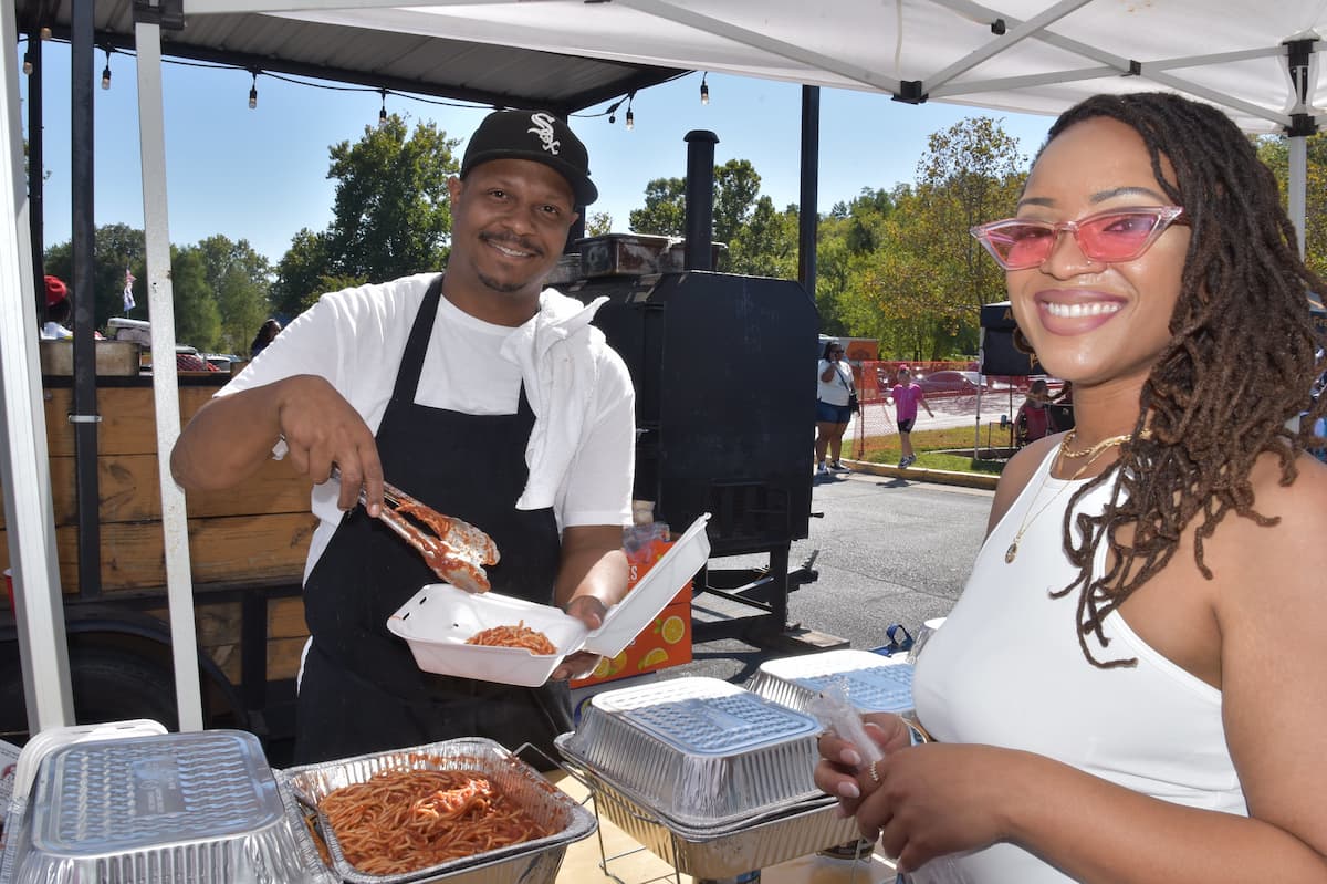 Two Lincoln University alumni hold food while outside during a Homecoming tailgate celebration.