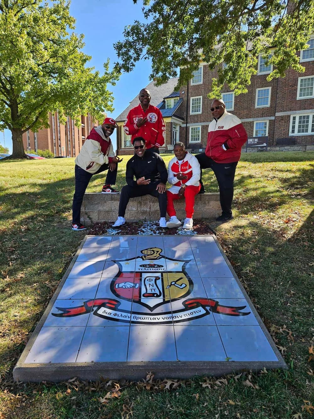 Lincoln University of Missouri Kappa alumni members pose for a group photo in red shirts next to their fraternity logo.