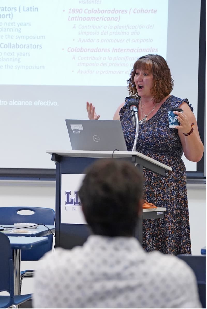 Woman stands behind podium with her mouth open and arms raised