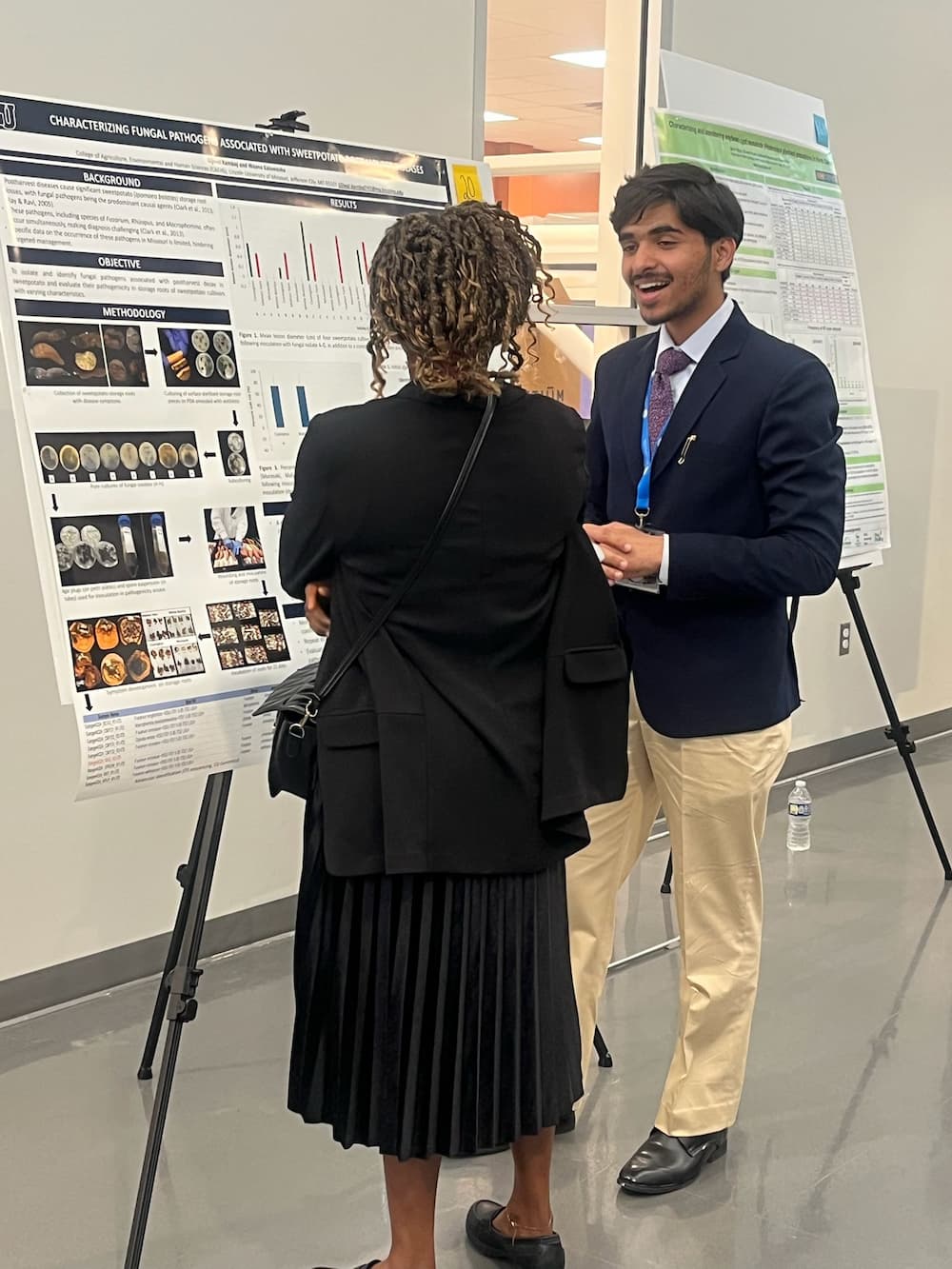 A man with his mouth open and woman with her back to the camera stand in front of a poster.  