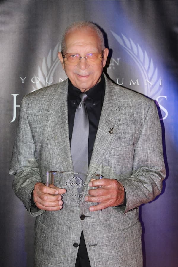 Ollie Gates Sr. stands in a suit with his Legend Award received during the 2025 Young Alumni Honors Awards.