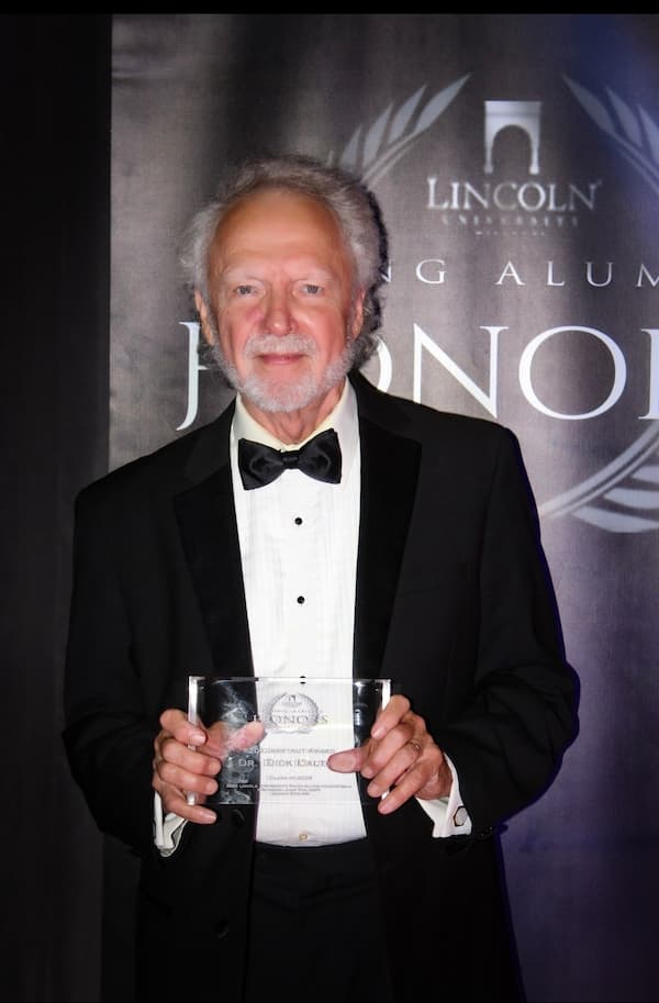 Dr. Dick Dalton stands in a suit with his award from the Young Alumni Honors Awards 2025 ceremony.