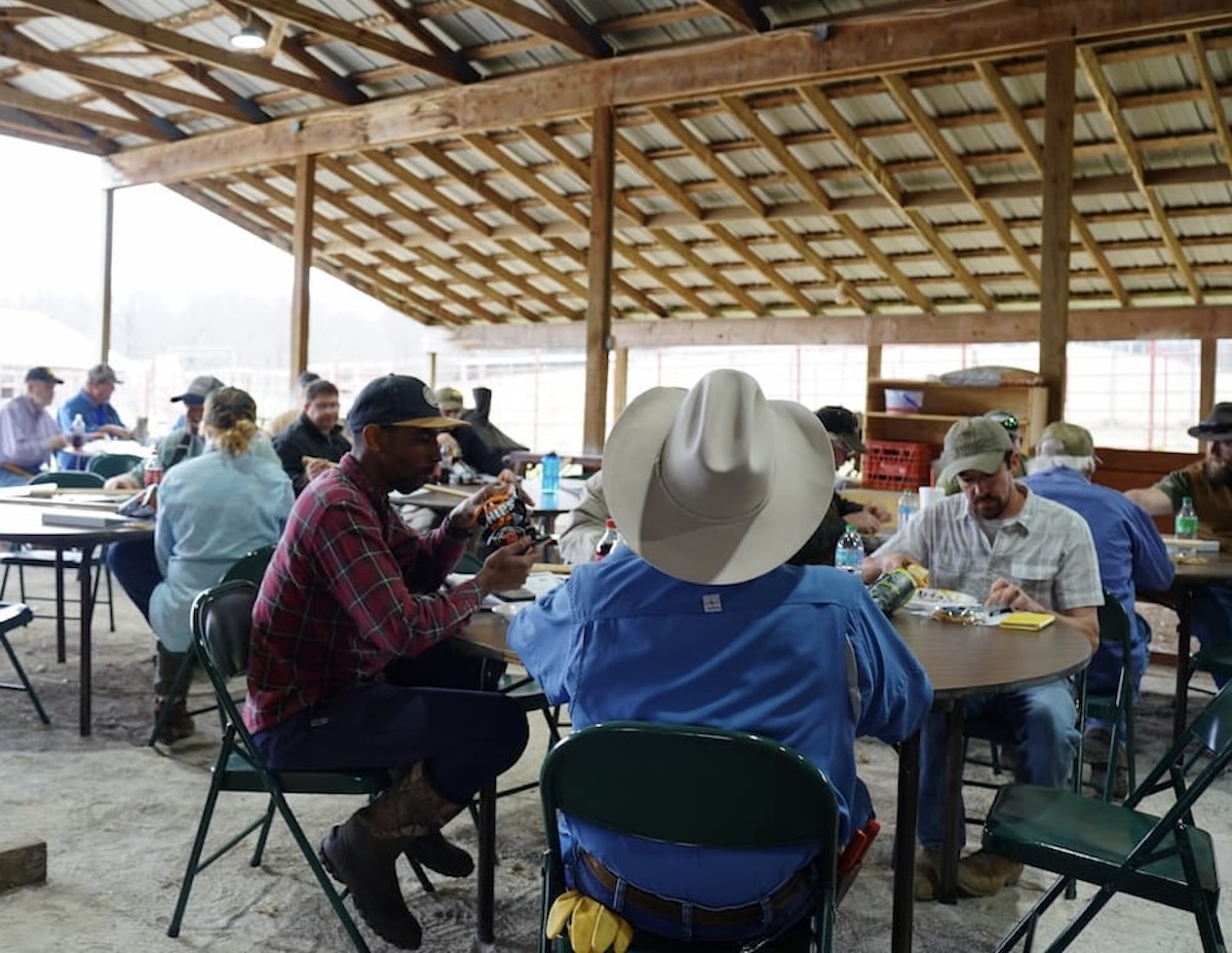 People wearing hats sit at round tables on folding chairs.