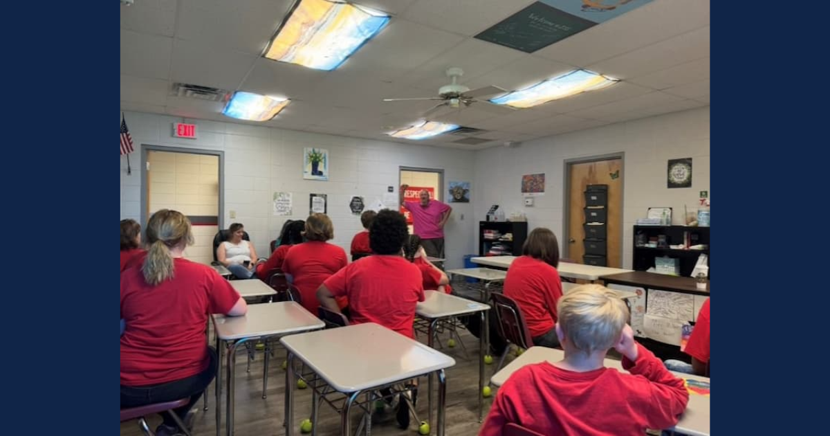 A man stands in the doorway of a classroom full of children