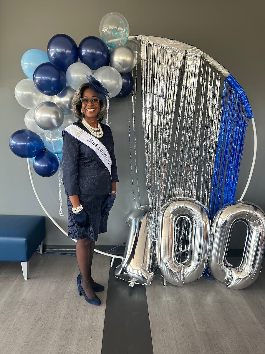 Staci Garrett Oliver stands in a navy dress with her Miss Lincoln sash next to decorations for the crowning of the 100th Miss Lincoln.