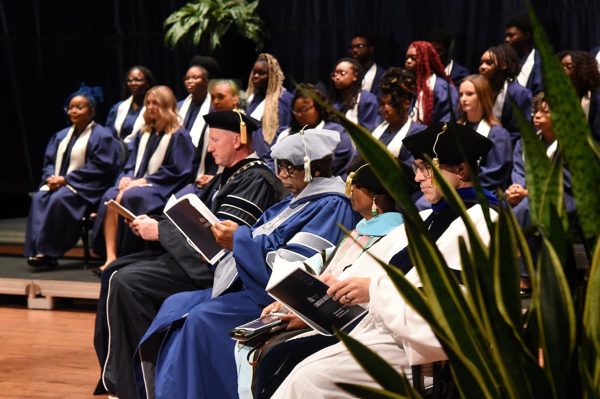 Lincoln University faculty and staff in academic regalia sit in chairs on the stage during Opening Convocation.