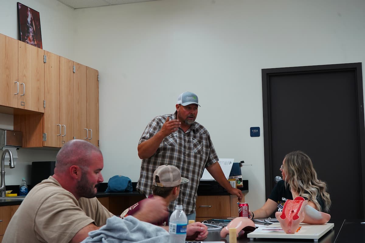 A man stands in front of a group of people sitting around a table.