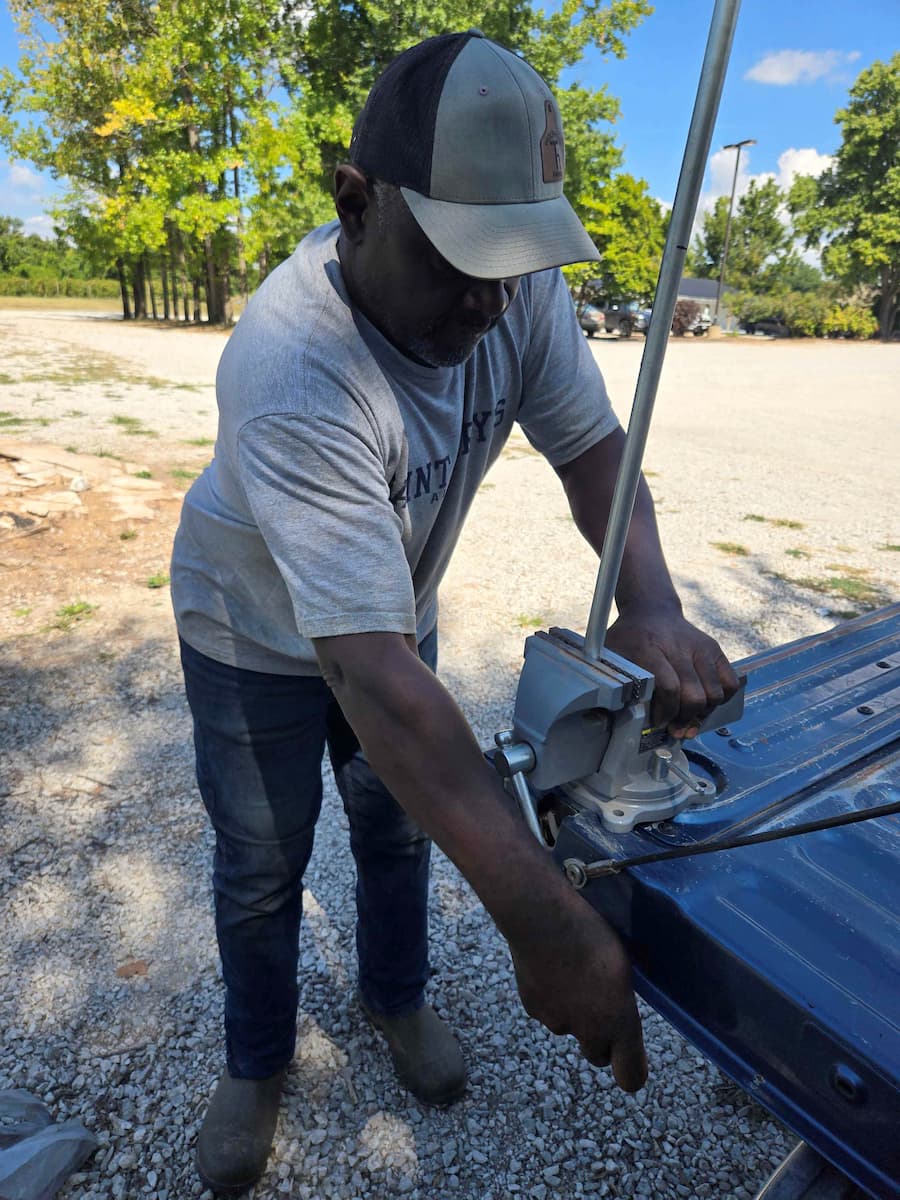 Tony White, an ISFOP participant working with farm outreach worker Mary Keeter, crimps the end of a low tunnel hoop with a vise to prepare it for installation.