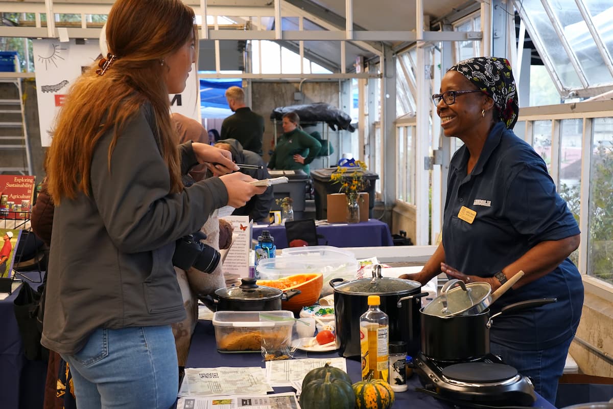 A woman smiles from behind a table of pumpkin dishes as she speaks with an attendee