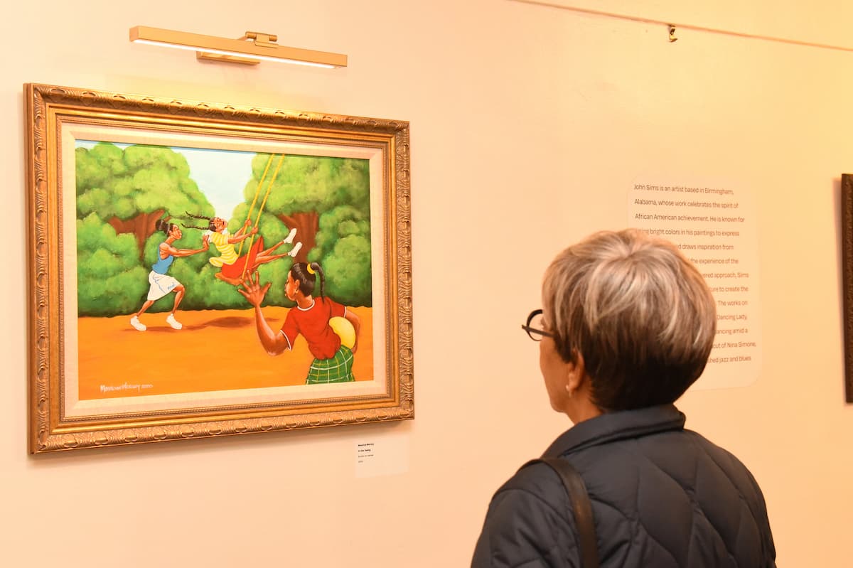 A woman stands with her back to the camera while she admires a painting on the wall.