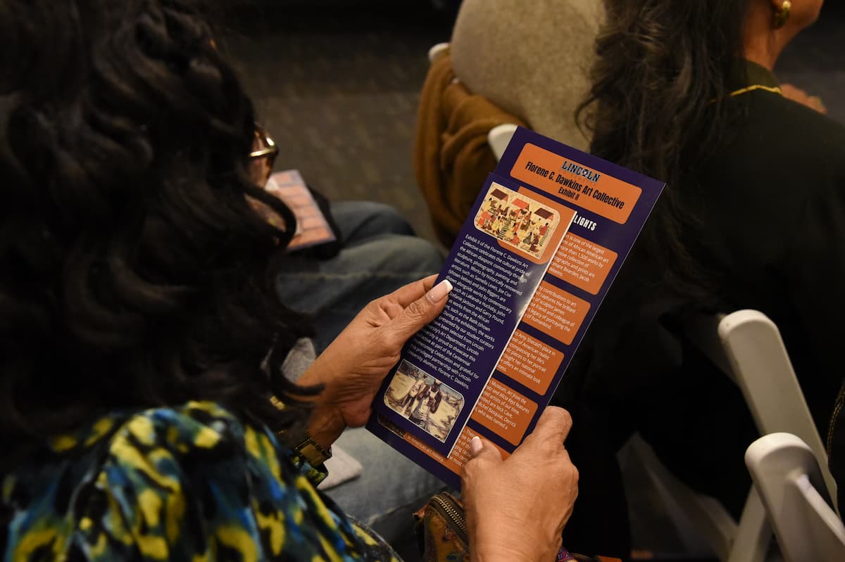 A woman sits while reading a pamphlet about artwork at the Florene Dawkins exhibit.