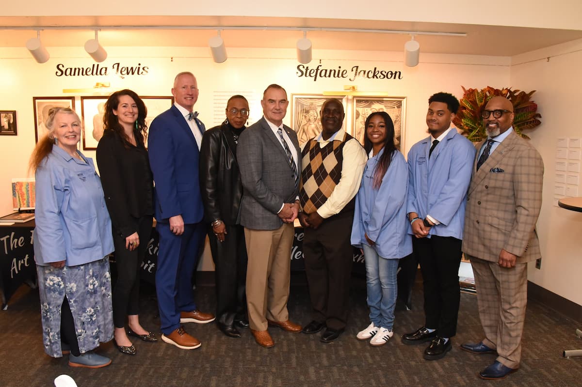 Well-dressed people stand in a line for a photograph during an art exhibit.