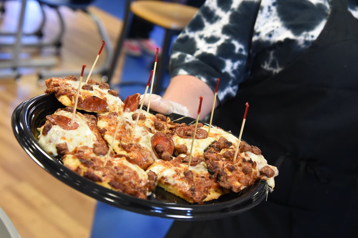 Pizza with pepperoni and sausage sits on a black platter.