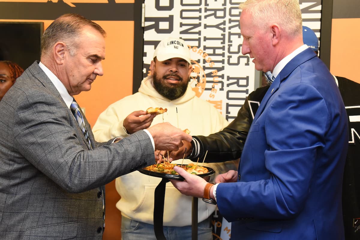 Three man take pizza from a platter at the Slim & Husky's grand opening on the Lincoln University campus.