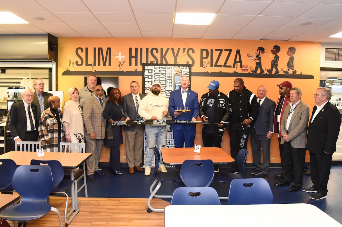 A group of people stand in a line while holding a plaque during the Slim and Husky's Pizza grand opening at Lincoln University.