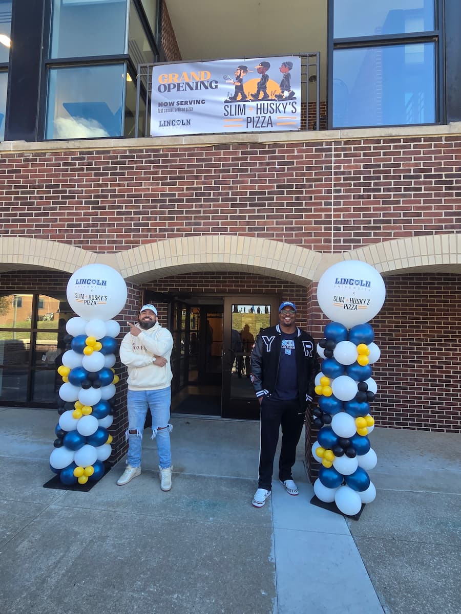 The Slim and Husky's Pizza owners stand by LU-branded balloons before the entrance to the SUC cafeteria.
