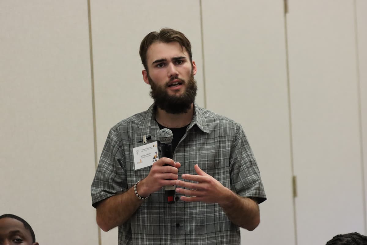 A young man stands speaking with a microphone in his hand.